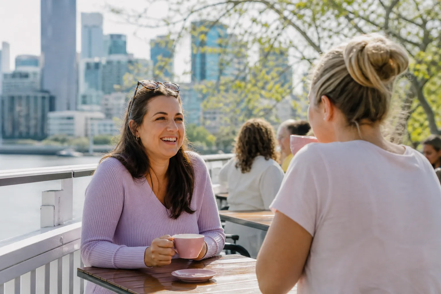 Two women chatting over coffee beside the Brisbane River
